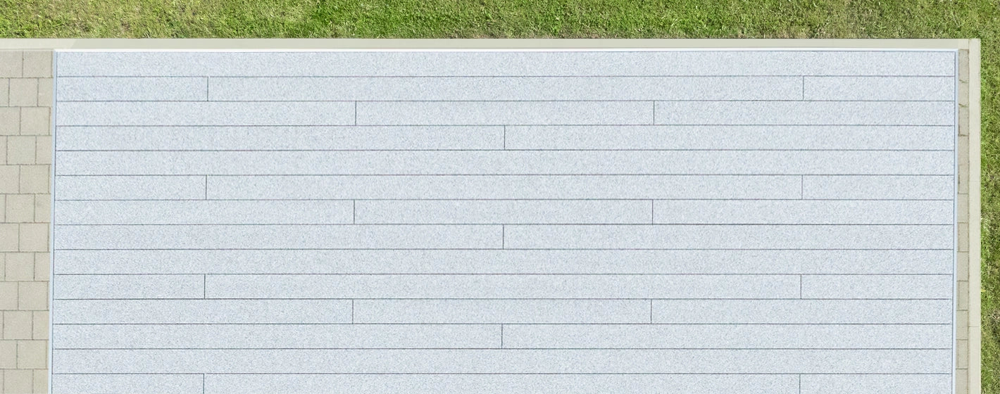 Vogelperspektive auf fertig verlegte Aluminium-Terrassendielen mit grau-weißer balkoFLOOR Granitoberfläche und exaktem, versetztem Fugenbild auf einer Rasen- und Pflasterfläche