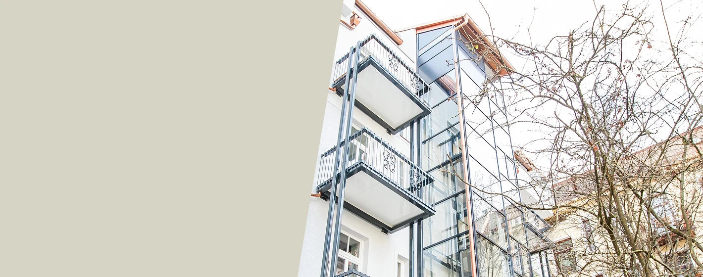 Modern saniertes Mehrfamilienhaus mit angebauten Balkonen und Aufzugsturm aus Glas zur Veranschaulichung moderner Balkonsanierungen und Terrassenprojekte