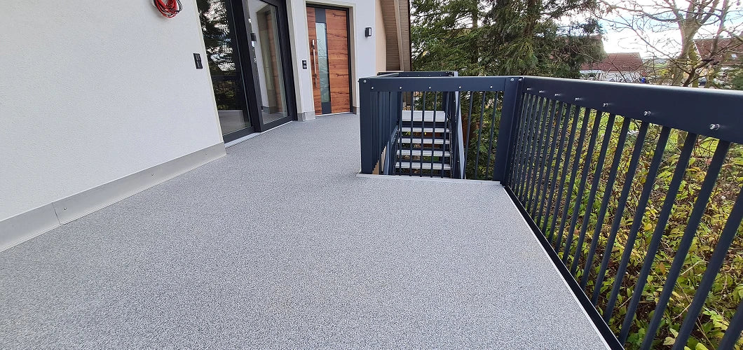 Fertig verlegte Terrasse mit rutschfestem balkoFLOOR Belag in Grau-Weiß, modernem anthrazitfarbenem Aluminium-Geländer und integriertem Treppenabgang
