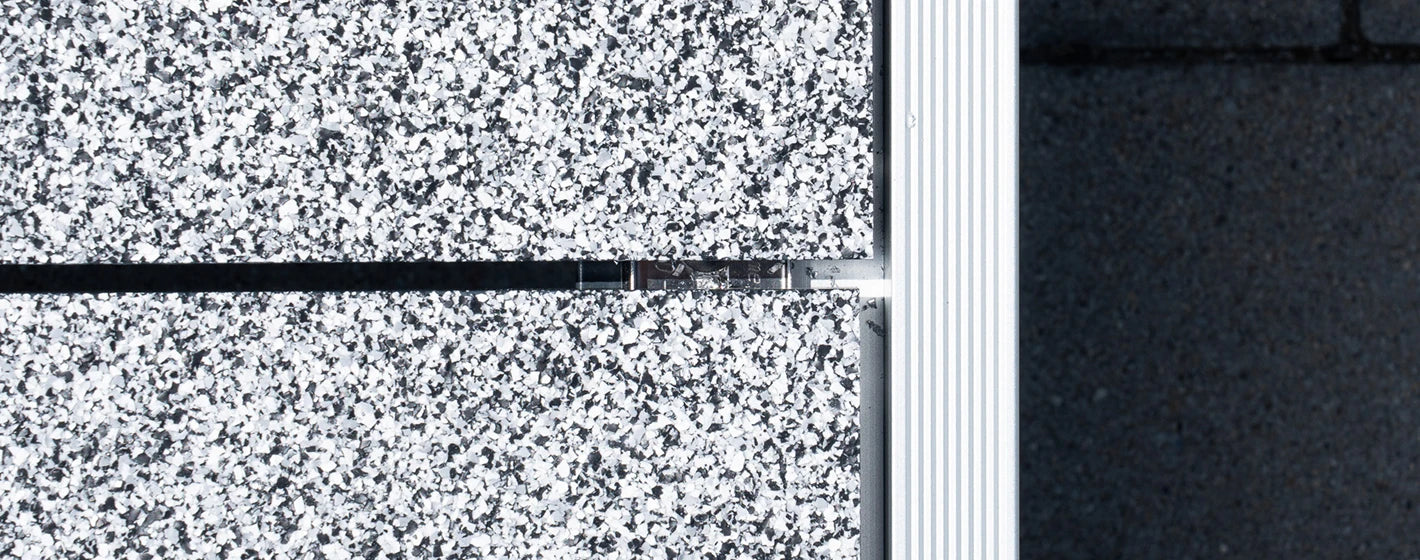 Detailaufnahme von oben auf zwei verlegte balkoFLOOR Aluminium-Terrassendielen in grau-weißer Granit-Optik mit präziser Fugenführung und silbernem Kantenabschlussprofil
